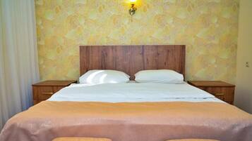 Habitación de hotel con cabecera de madera, dos mesitas de noche, cama con ropa blanca y un estampado de flores en el papel tapiz.