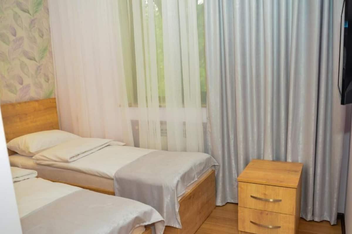 A room with two beds, a wooden nightstand with drawers, and a TV mounted on the wall.