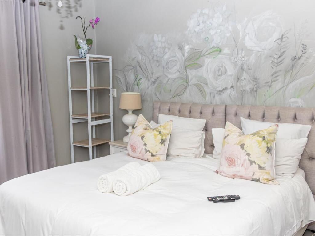 Una cama bien hecha con almohadas florales, una lámpara de noche y un control remoto sobre la cama.