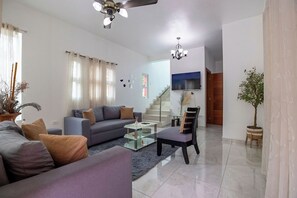 Un salon comprenant un canapé, un fauteuil, une table basse et un téléviseur fixé au mur.