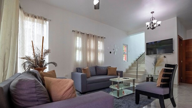 Un salon moderne avec un canapé, un fauteuil et une table basse, un escalier et un téléviseur fixé au mur.