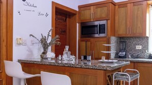 Une cuisine dotée de meubles en bois, d’un four à micro-ondes en acier inoxydable, d’un comptoir en granit et d’un coin bar avec des chaises blanches.