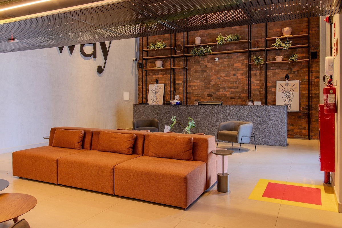 A modern lobby with a large sofa, a reception desk, and shelves with plants.