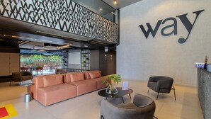 Un vestíbulo moderno con un gran letrero que dice 'way', un área de estar con sofás y sillones, y vistas al comedor con mesas y sillas.