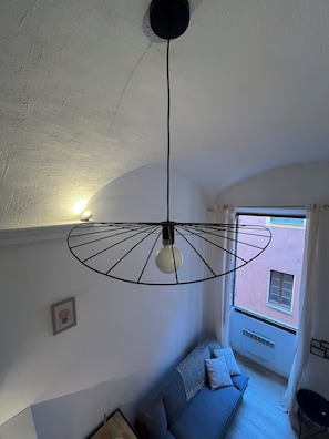 Ein Zimmer mit Deckenventilator, einer Hängelampe, einer Couch und einem Fenster mit Blick auf ein Gebäude.