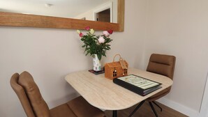A dining area with a table, chairs, a vase with flowers, a basket, and a framed certificate. - Little Holm Garth (Whitby)