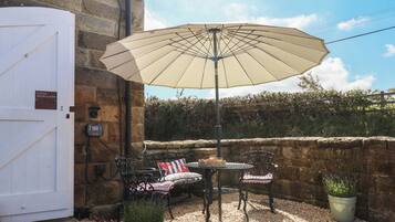 A patio with a table and chairs, a large umbrella, a potted plant, and a stone wall.