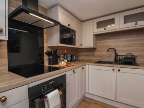 A modern kitchen with white cabinetry, a black stove, a microwave, and a sink. - Little Holm Garth (Whitby)