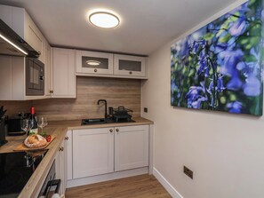 A modern kitchen with white cabinetry, a wooden countertop, a built-in oven, and a wall-mounted picture of flowers. - Little Holm Garth (Whitby)