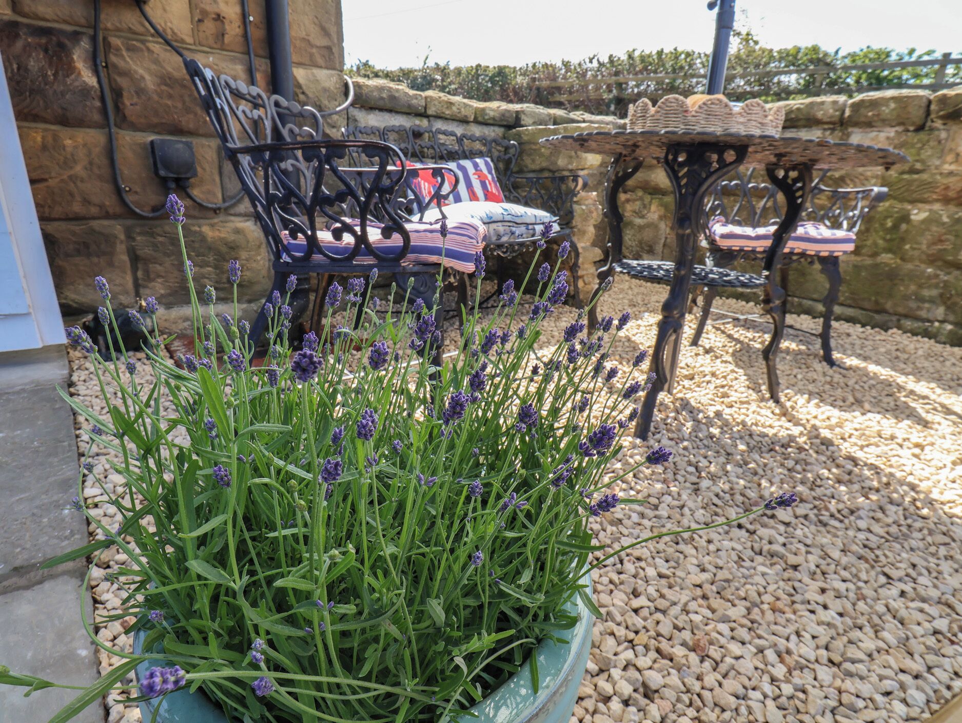 Terraza al aire libre con pared de piedra, planta de lavanda en maceta y suelo de grava.