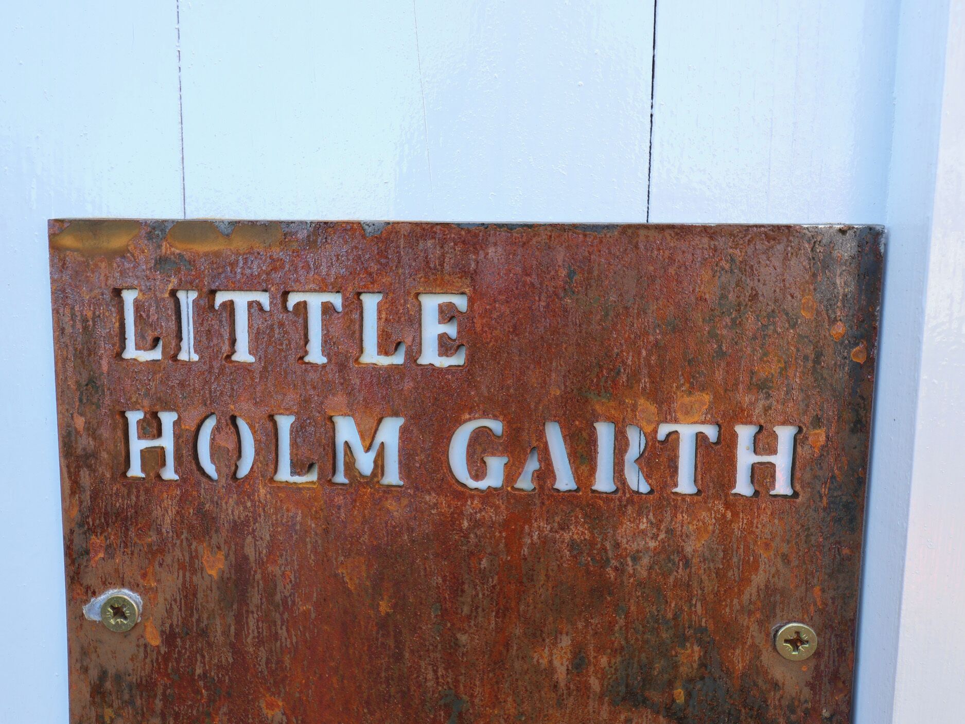 En rusten metalskilt med teksten 'LITTLE HOLM GARTH'.