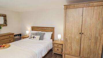 A bedroom with a wooden bed, two bedside tables with lamps, a wooden wardrobe, and a wicker basket with bread on the bed.