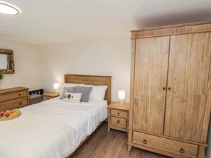 Quarto com cama de madeira, duas mesas de cabeceira com abajures, guarda-roupa de madeira e uma cesta de vime com pão na cama.