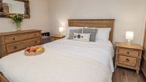 A neatly arranged bedroom with a wooden headboard, a bed with white bedding, two bedside tables with lamps, a nightstand with a lamp, a dresser, and a basket of fruit on the bed. - Little Holm Garth (Whitby)