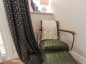 Una silla con cojín, una cortina estampada y una estantería con libros y una lámpara.