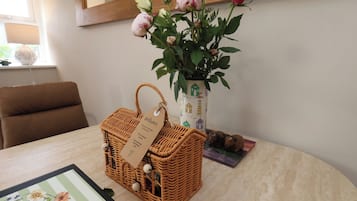 Uma cesta de vime com uma etiqueta, um vaso com rosas e uma placa de boas-vindas emoldurada sobre uma mesa.