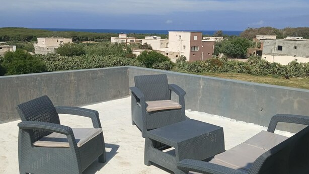 A rooftop terrace with wicker furniture and a view of the sea and buildings.
