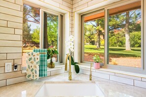 Ein Badezimmer mit einem großen Waschbecken, zwei goldenen Wasserhähnen und Blick auf einen Golfplatz durch große Fenster.