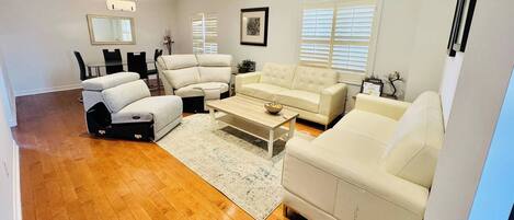 A living room with a sofa, armchairs, a coffee table, a rug, a dining table, chairs, a chandelier, and a framed picture on the wall.