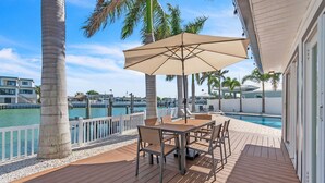 A wooden deck with a table and chairs, a pool, and a view of the water and buildings. - Palms of the Isles (St. Petersburg)