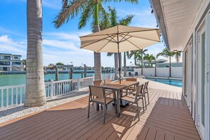 Eine Holzterrasse mit Tisch und Stühlen, ein Pool und Blick auf Wasser und Gebäude.
