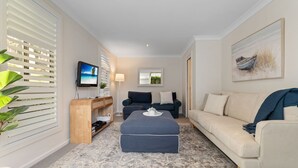 Sala de estar com televisão, sofá, pufe e planta.