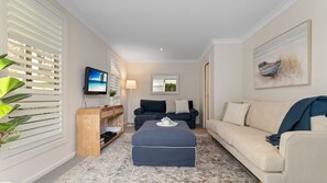 A living room with a TV, sofa, ottoman, and a plant. - Flannel Flower Beach House (Shoal Bay)