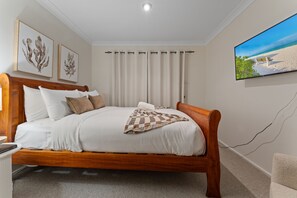 A bedroom with a wooden bed, white bedding, a checkered throw, and a beach scene painting. - Flannel Flower Beach House (Shoal Bay)