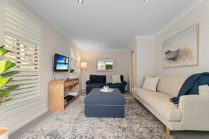 A modern living room with a flat-screen TV, a sofa, a coffee table, and a painting on the wall. - Flannel Flower Beach House (Shoal Bay)