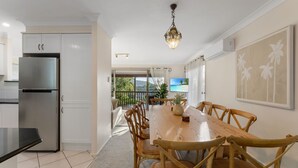 Cozinha moderna com frigorífico de aço inoxidável, mesa de jantar de madeira com cadeiras e vista para o exterior.