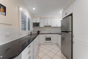 A modern kitchen with white cabinets, a stainless steel refrigerator, a built-in oven, and a microwave. - Flannel Flower Beach House (Shoal Bay)