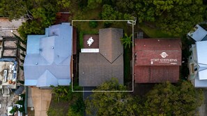 An aerial view of a residential area with a prominent building labeled 'PORT STEPHENS ACCOMMODATION' and a rooftop terrace with outdoor furniture. - Flannel Flower Beach House (Shoal Bay)