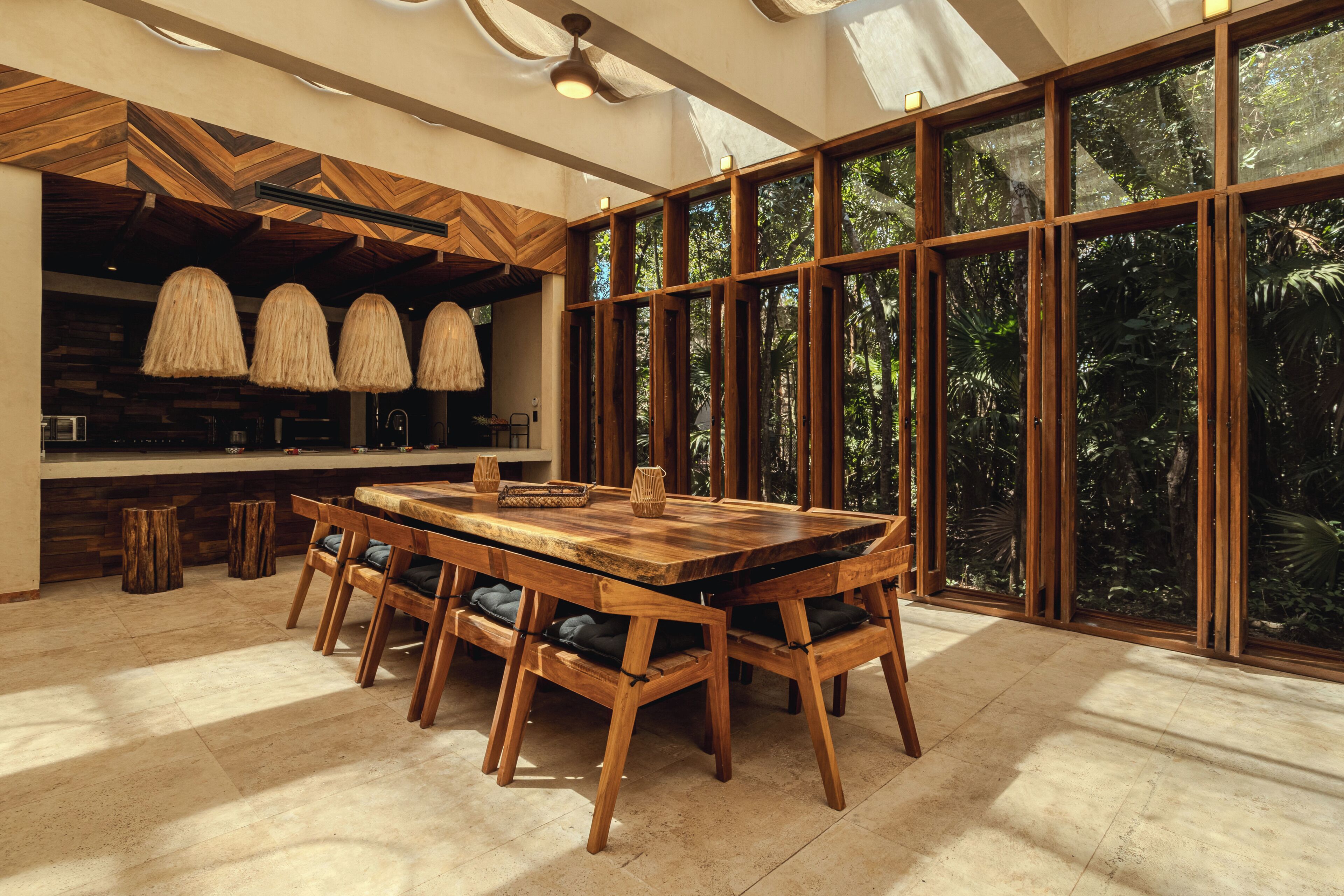 Un vaste espace à manger avec une grande table et des chaises en bois, une cuisine dotée d’un plafond en chevrons et de grandes fenêtres offrant une vue sur l’extérieur.