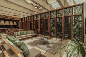 A spacious living area with a large window, a sofa set, a coffee table, and a dining area with wooden furniture. - Luxury in Bacalar whit Private Dock (Buenavista)