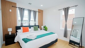 Moderni hotellihuone, jossa on suuri sänky, yöpöytä lampun kanssa, peili ja näkymä ulos.