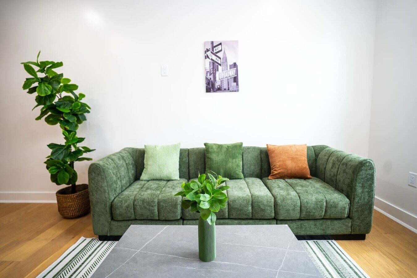 Ein grünes Sofa mit drei Kissen, einem Blumentopf und einem gerahmten Bild an der Wand.