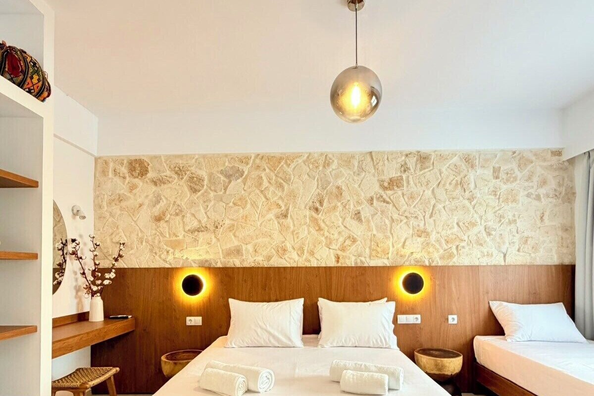 Ein Hotelzimmer mit einem großen Bett, zwei Nachttischen, einem Holzkopfstück, einer Steinwand und einer Hängeleuchte.