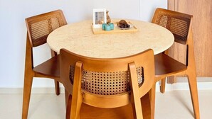 A round wooden table with two chairs, a door, and a wall-mounted light switch. - Kapetánissa Concept Studios (Stalida)