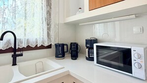 A compact kitchen with a sink, a coffee maker, a microwave, and wooden cabinets. - Kapetánissa Concept Studios (Stalida)
