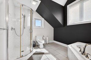 A modern bathroom with a glass shower enclosure, a white toilet, a bathtub, and a window providing natural light.