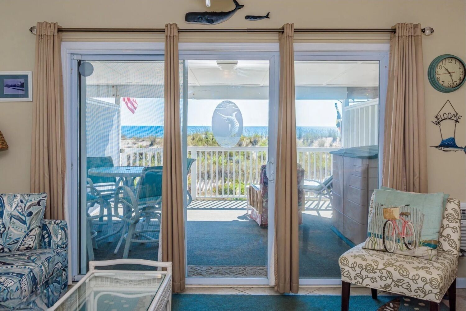 Quarto com porta de correr de vidro que dá para uma varanda com móveis de exterior, relógio e um objeto decorativo na parede.