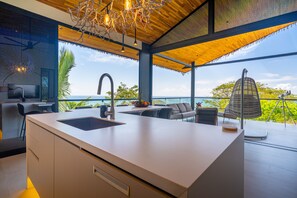 A modern kitchen with a large island, a dining area with outdoor seating, and a view of the ocean. - Stealing Time Costa Rica (Esterillos Oeste)