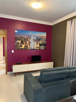 A living room with a large cityscape painting, a flat-screen TV, a wooden console, and a grey sofa. - LK Grajaú 5 (Belo Horizonte)