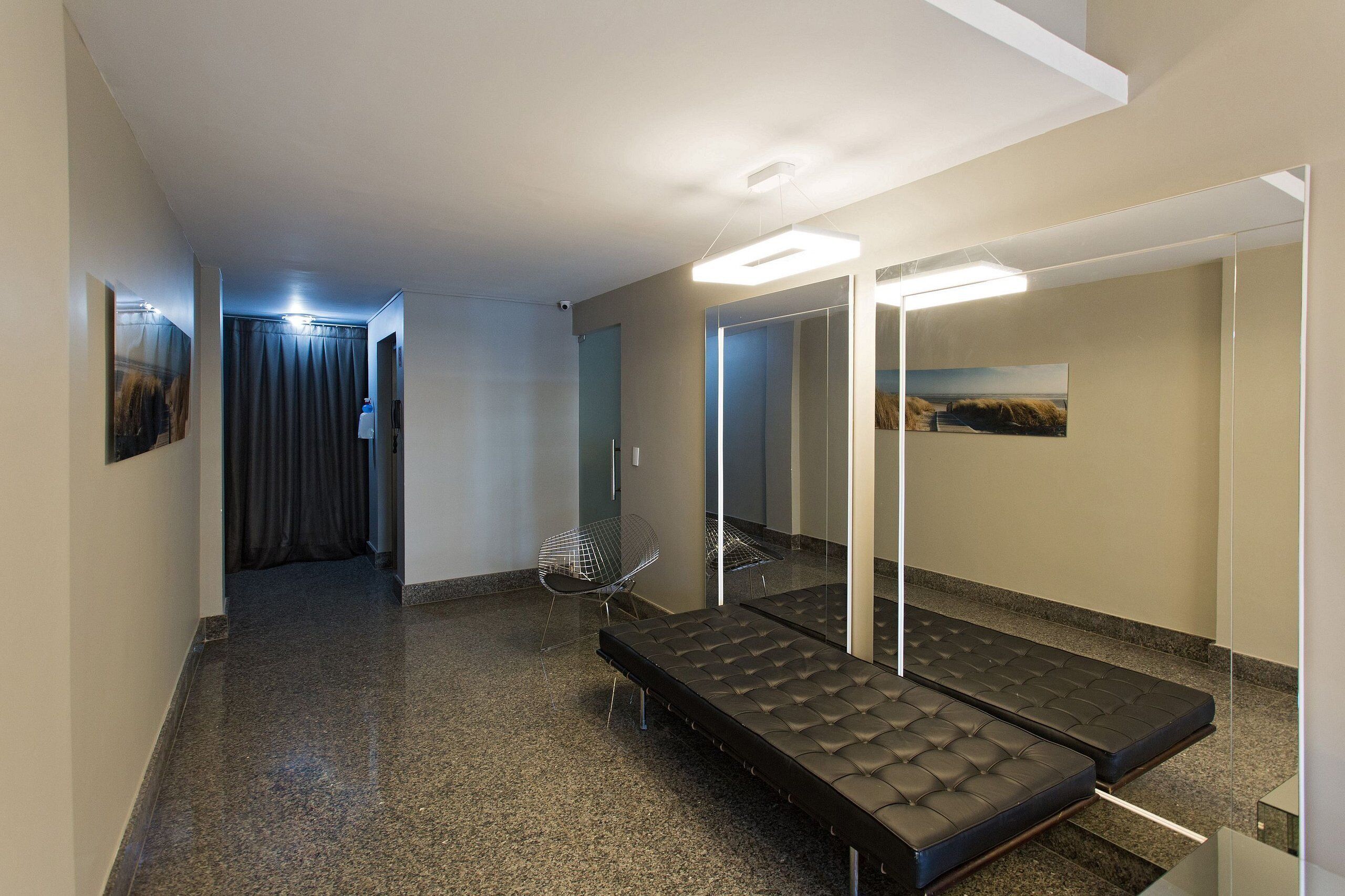 A hotel room with a bed, a chair, a mirror, and a hallway leading to another room.