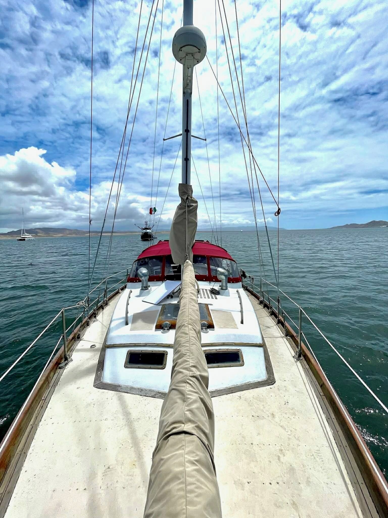 Dek van een boot met een stuurwiel, een rood zonnescherm en uitzicht op zee en verafgelegen land.