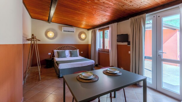 Une pièce avec un lit, une table avec des assiettes, un plafond en bois et une fenêtre avec des rideaux.