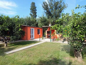 A small orange building with a door and windows, surrounded by greenery and trees. - L'Agrumeto-Casa Cedro. Porto Tramatzu beach (Teulada)