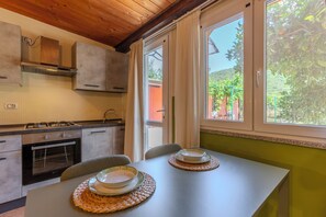 A kitchen with a dining table, cabinets, and a window with a view of greenery. - L'Agrumeto-Casa Cedro. Porto Tramatzu beach (Teulada)