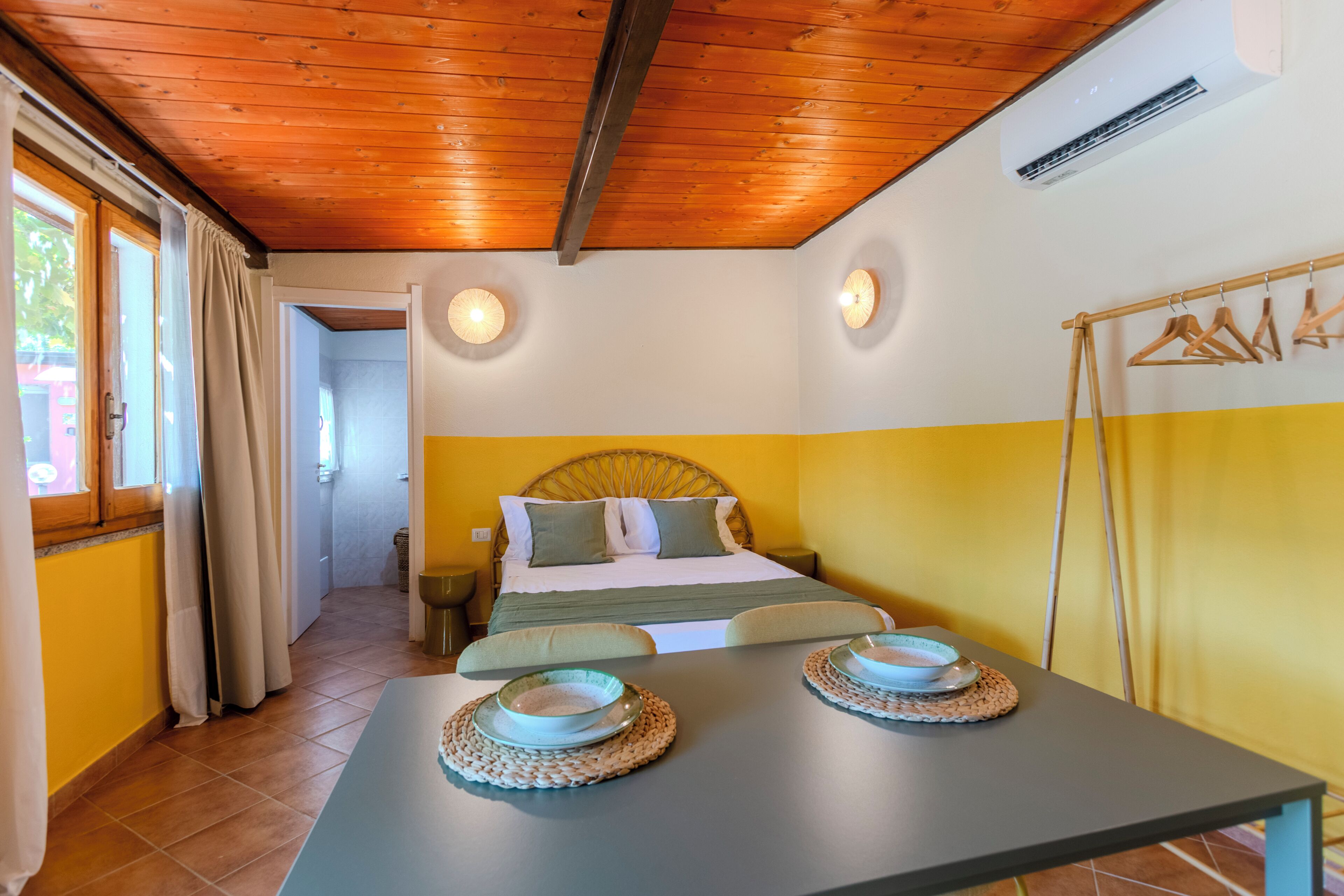 A room with a bed, a table with two bowls, a wooden ceiling, and a wall-mounted air conditioner.