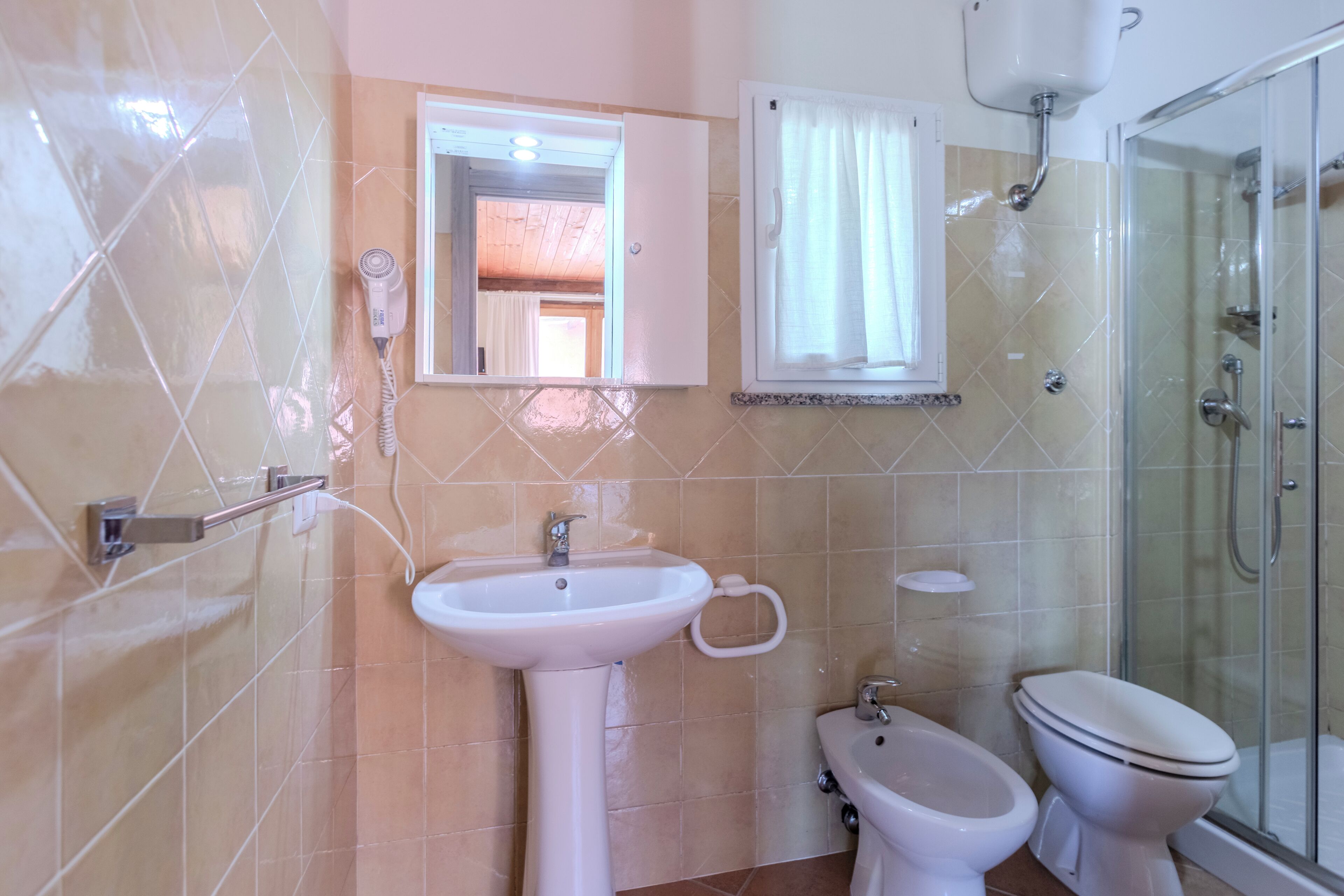 Baño con lavamanos, bidé, inodoro y cabina de ducha de vidrio.